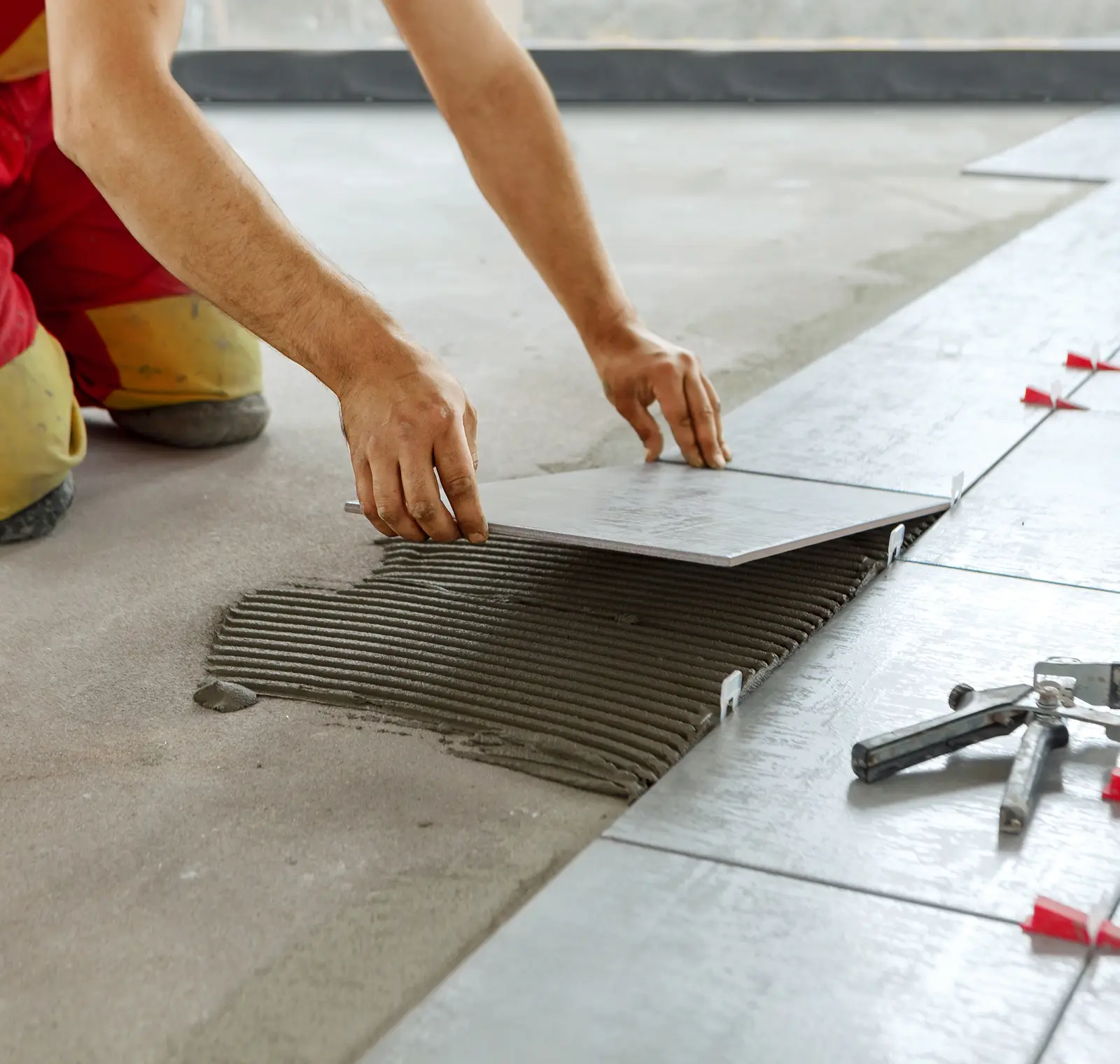 Person laying a large tile on a floor using adhesive, with tools nearby.